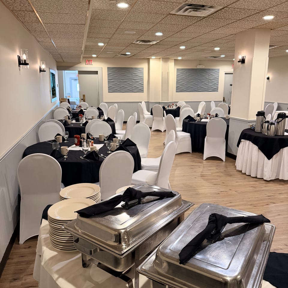 Elegant restaurant dining room with black-clothed tables, white chair covers, place settings, and covered buffet chafing dishes.