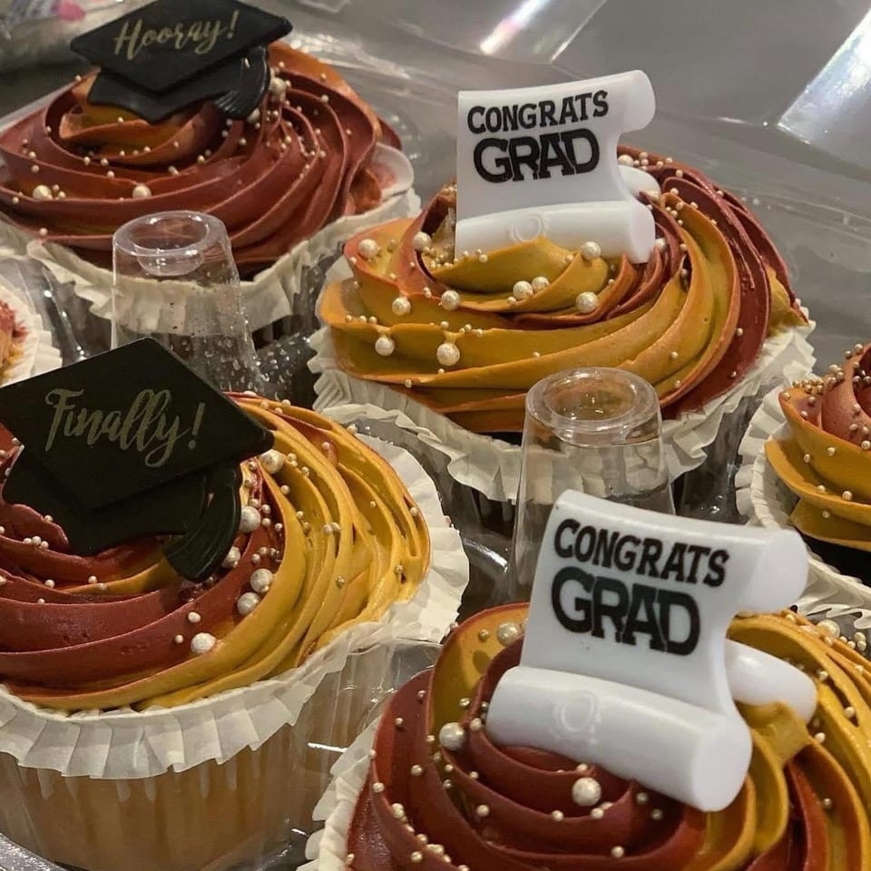Graduation-themed cupcakes with swirled burgundy and gold frosting, pearl sprinkles, and graduation cap and “Congrats Grad” toppers.