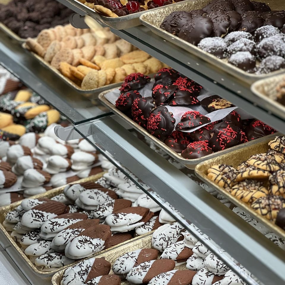 Display shelves hold trays of assorted decorated cookies, including chocolate-covered, cherry-topped, powdered, and striped varieties.