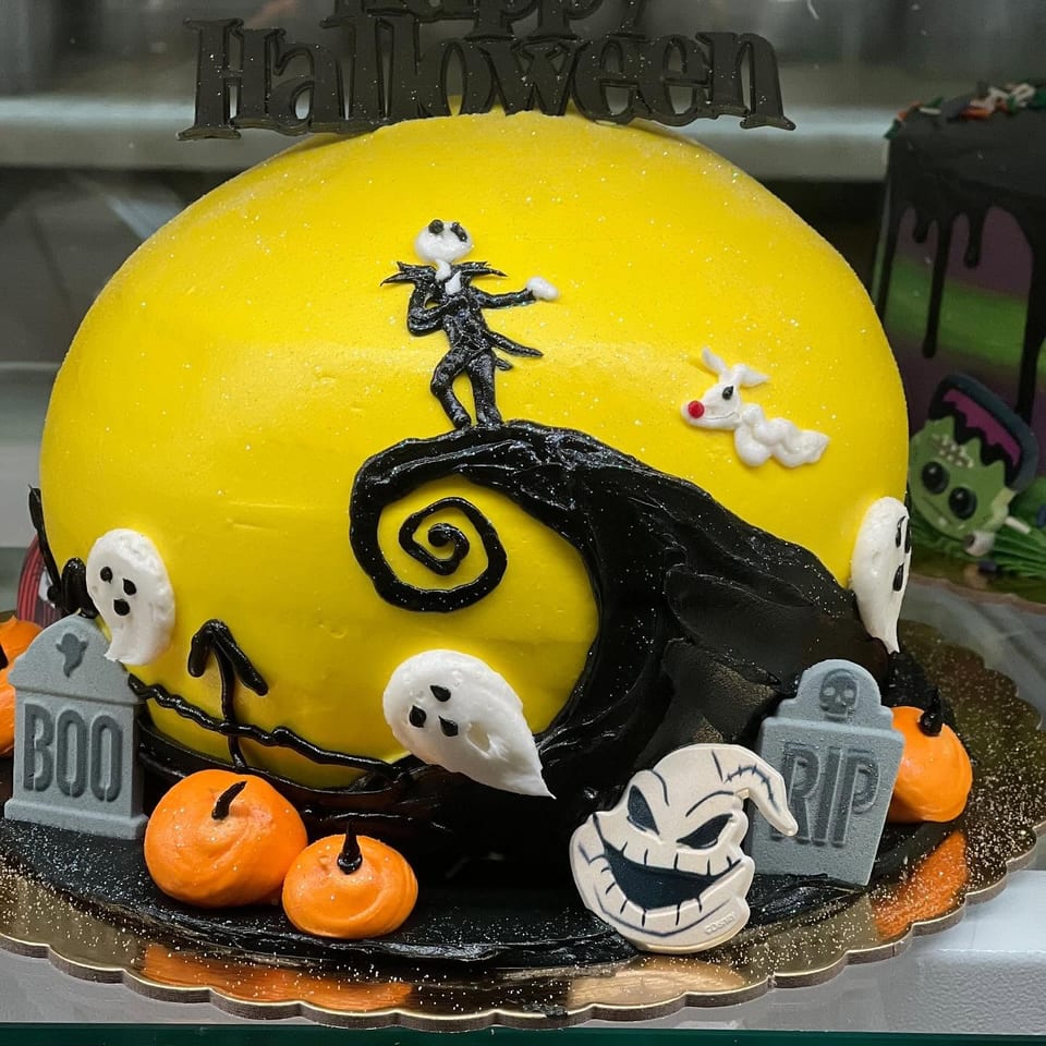 Halloween-themed yellow cake decorated with Jack Skellington, ghosts, pumpkins, gravestones, and a Happy Halloween topper.