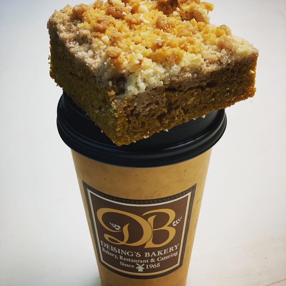 Crumb-topped coffee cake rests on a branded Deising’s Bakery takeaway coffee cup.