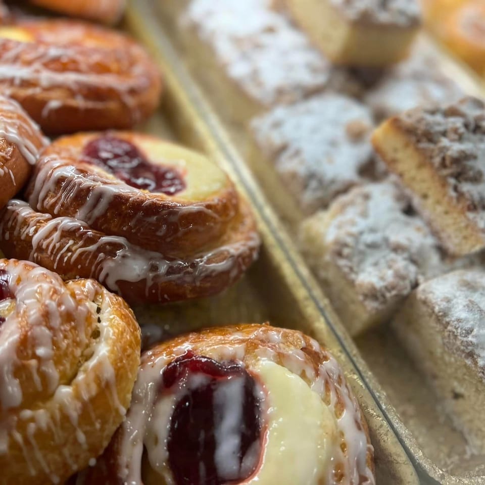 Glazed pastries filled with red jam sit beside powdered sugar-coated pastries on bakery trays.