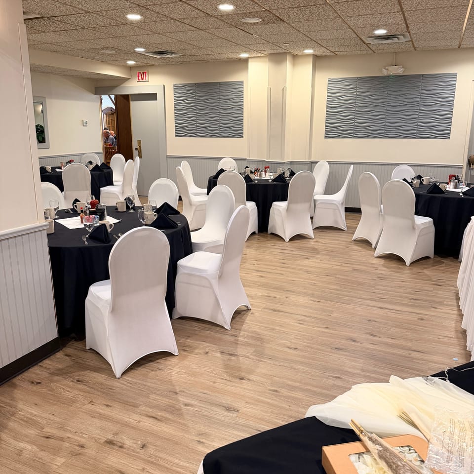 Elegant restaurant dining room with black-clothed tables, white-covered chairs, wavy wall panels, and wood flooring.