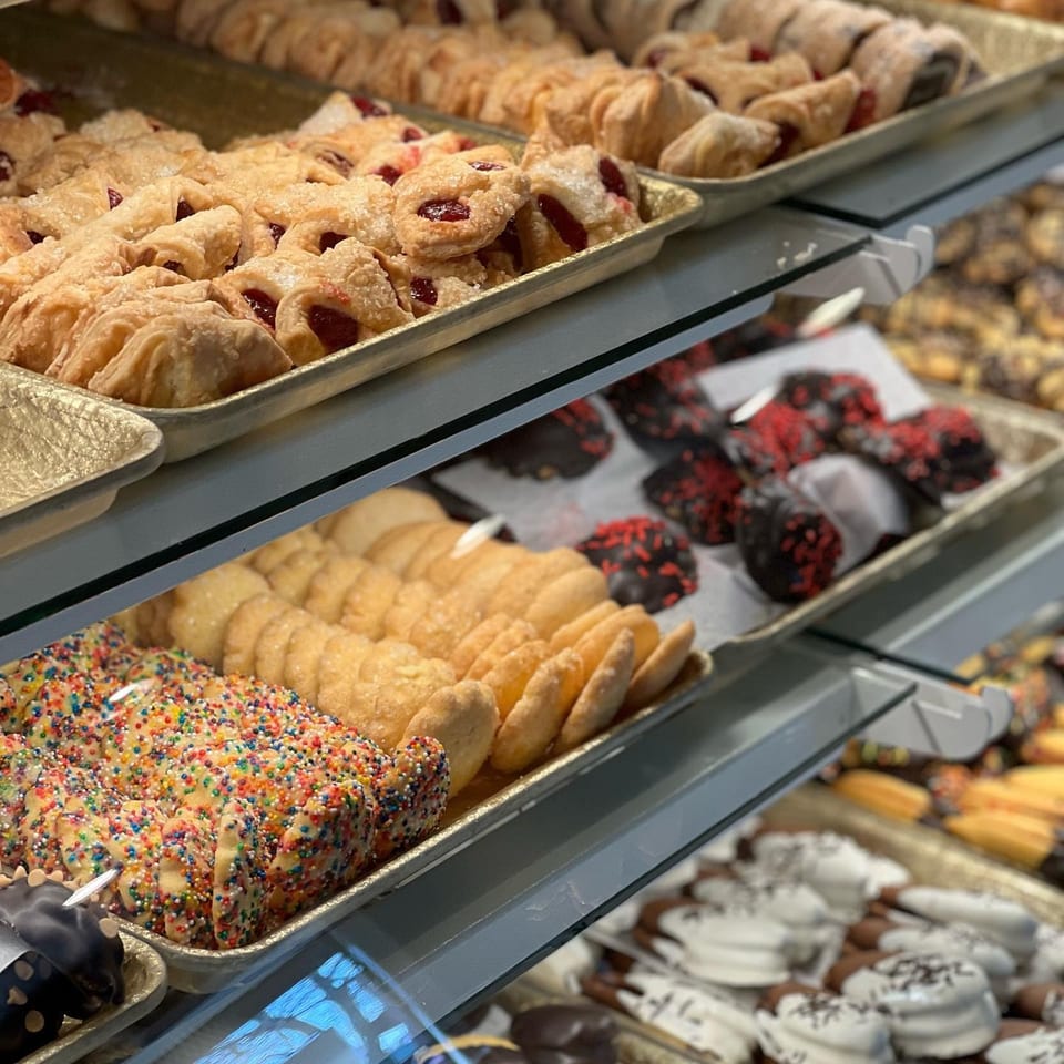 Bakery display case filled with fruit pastries, sugar cookies, sprinkle-covered treats, chocolate cookies, and assorted confections.