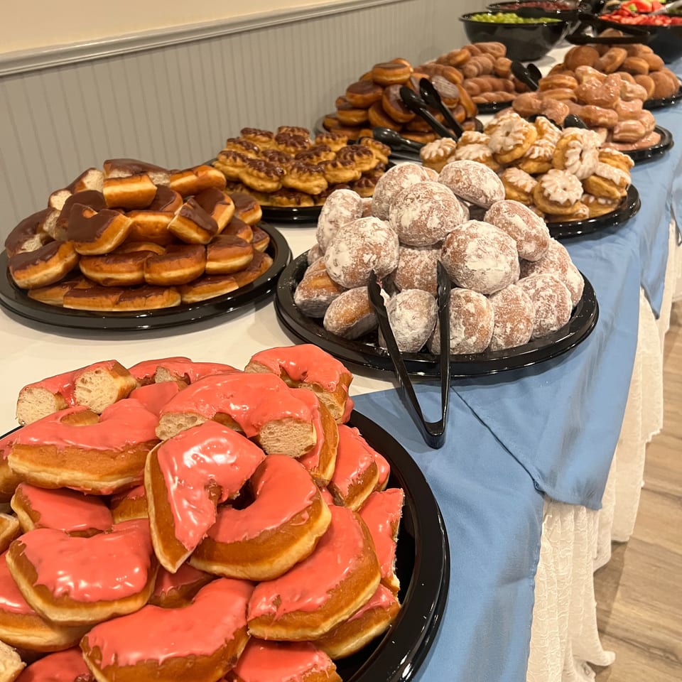 Buffet table displaying assorted doughnuts and pastries, including pink-glazed, chocolate-dipped, powdered, and cream-filled varieties.
