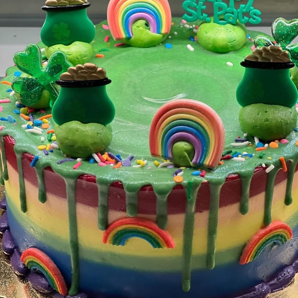 Colorful St. Patrick’s Day cake decorated with rainbows, green frosting, leprechaun pots, shamrocks, and a Happy St. Pats sign.